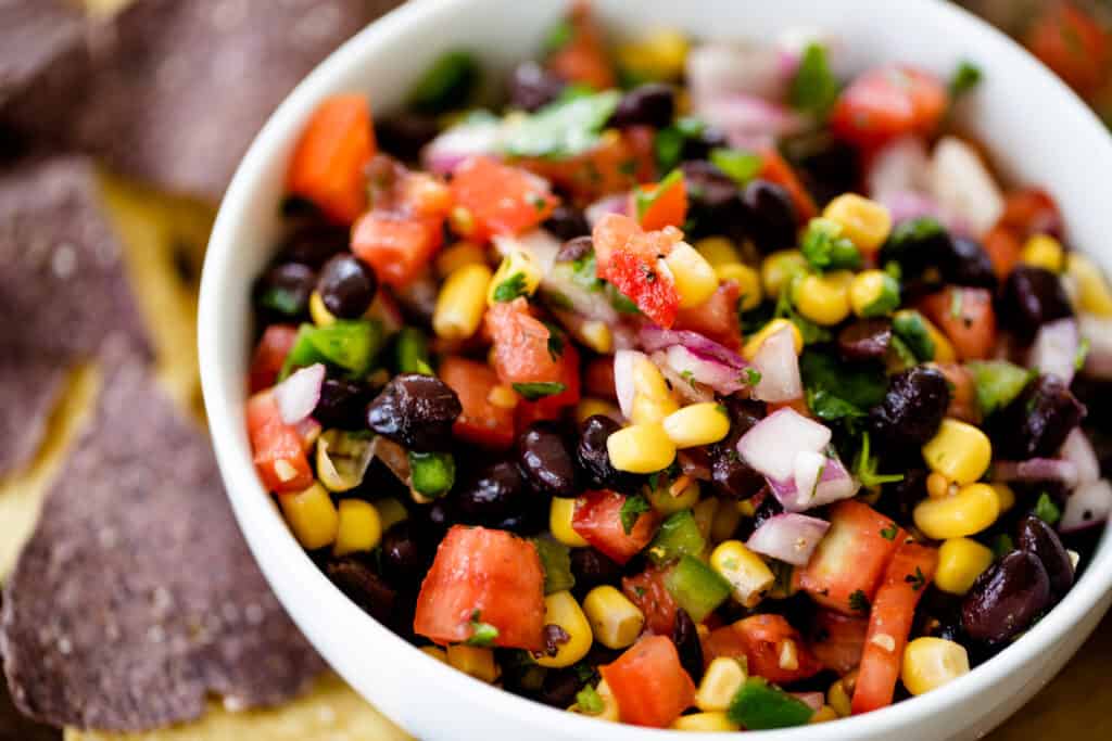 Bean and corn salsa sits in a serving bowl alongside blue corn chips.