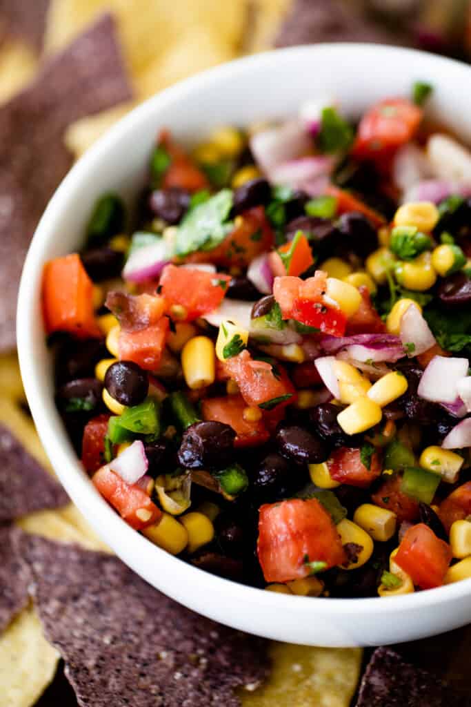 Bean and corn salsa sits in a serving bowl alongside blue corn chips.