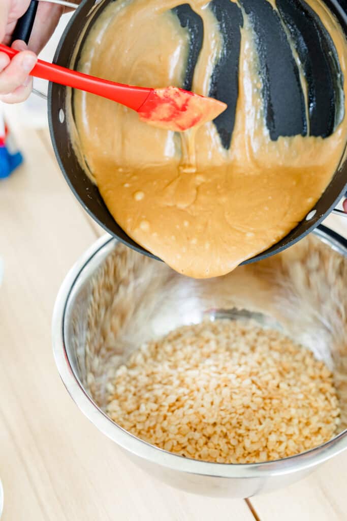 Pot of peanut butter syrup is being held over metal bowl with cereal to be poured.