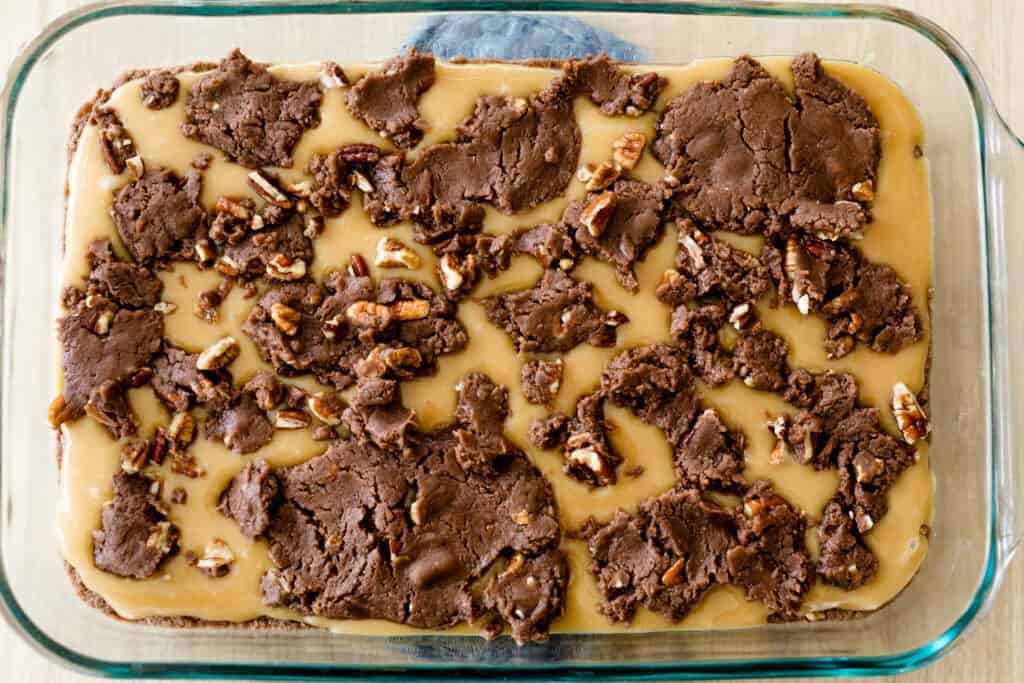 Brownie batter dough is dropped over the top of brownie bar caramel layer.