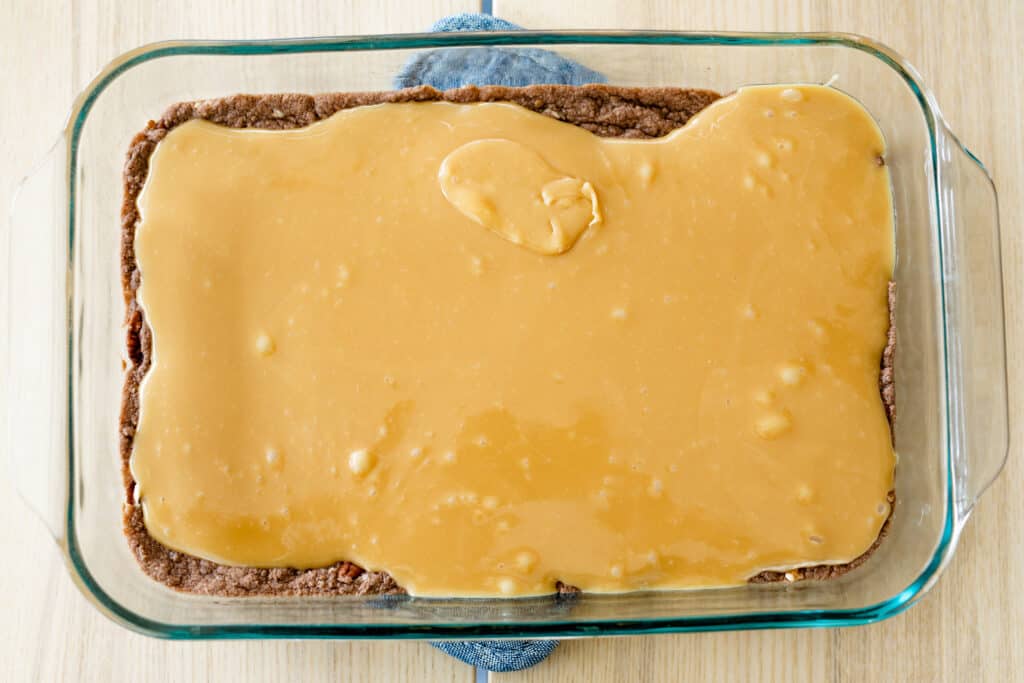 Caramel sauce is poured out and spread over the cooked brownie base layer.