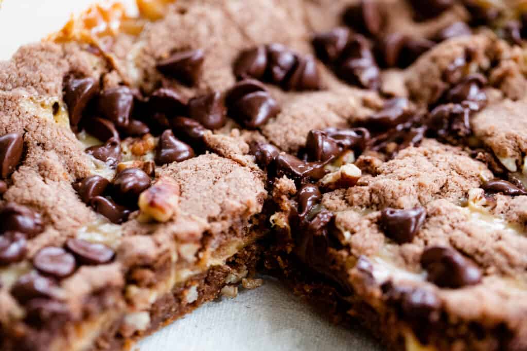 A glass pan sits on the counter displaying each delicious layer of german chocolate caramel brownie bar goodness.