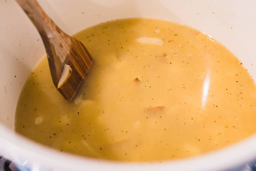 Wooden spoon stirs potato soup.