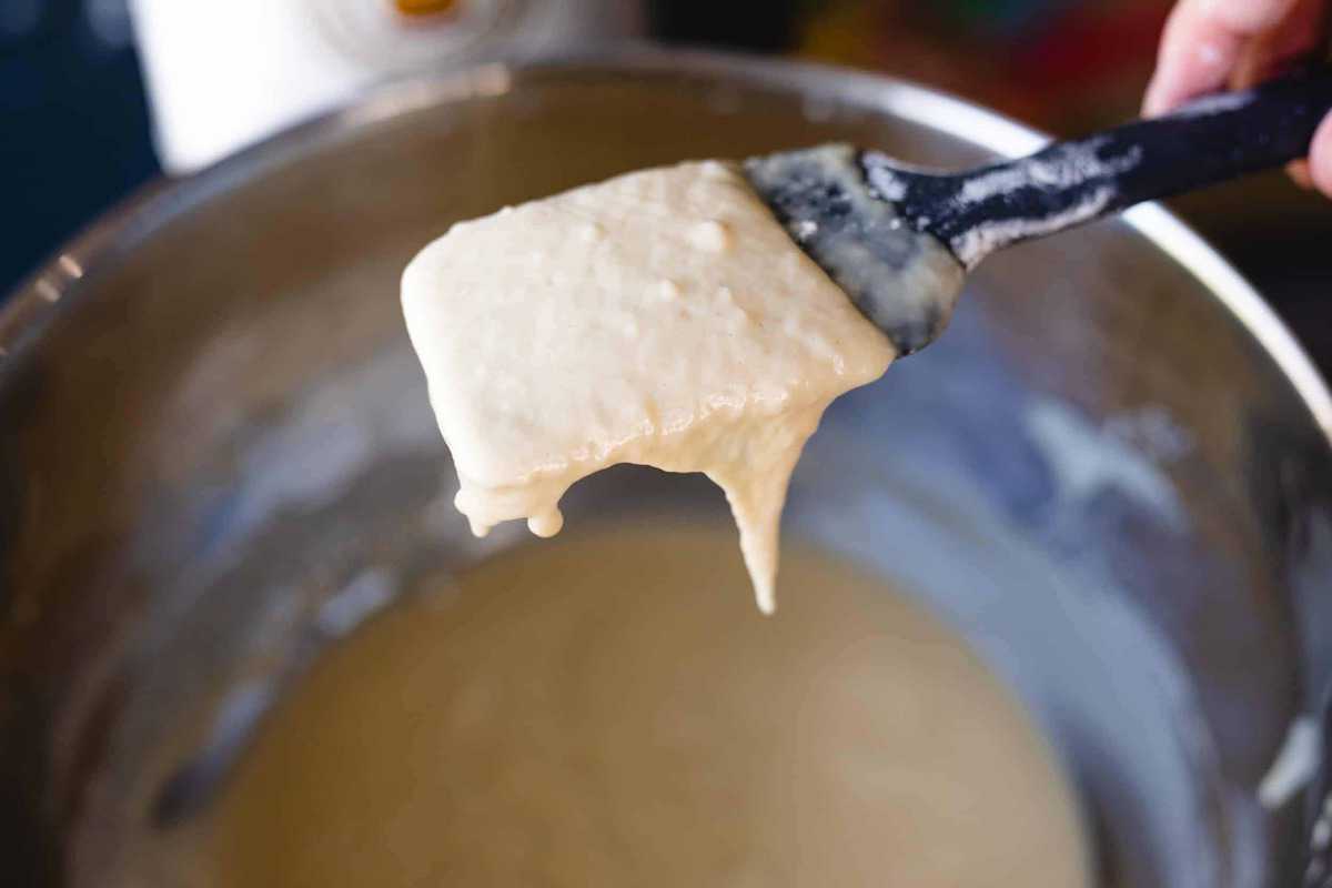 A spatula is held over a bowl of wet dough. The dough is wet and shiny, ready for more flour to be added.