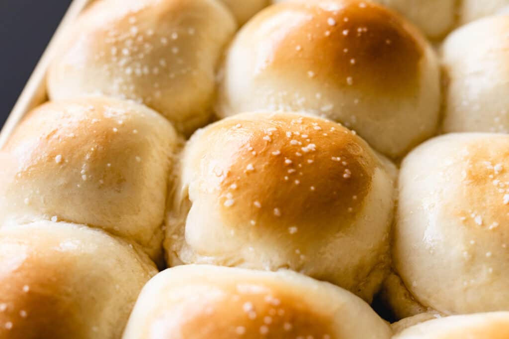 Perfectly golden brown rolls sit on a tray brushed with butter and topped with sea salt.