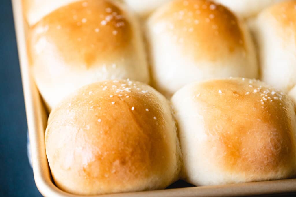 Soft dinner rolls on a corner of the baking sheet are golden brown and ready to enjoy.