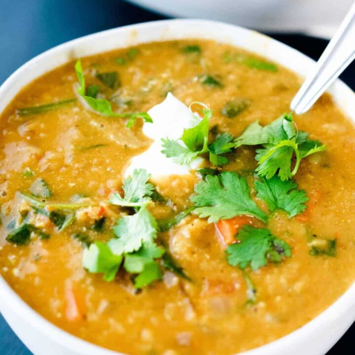 A bowl of soup sits on a table garnished with sour cream and fresh cilantro. A spoon sits in the bowl.