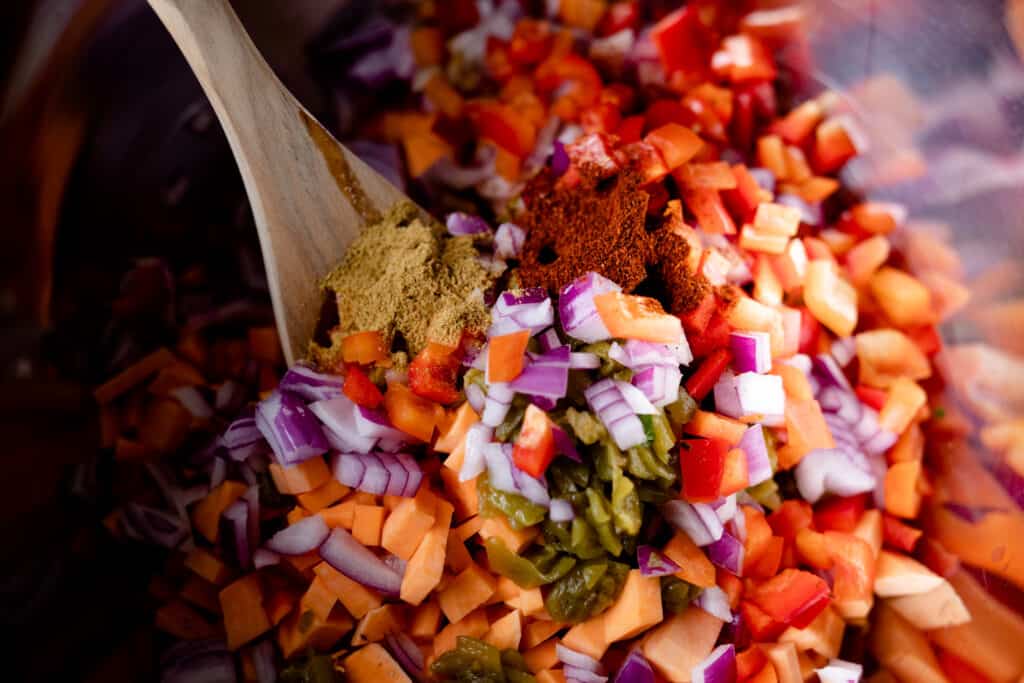Seasonings are added to a bowl of chopped veggies. A wooden spoon is ready to combine the mixture.
