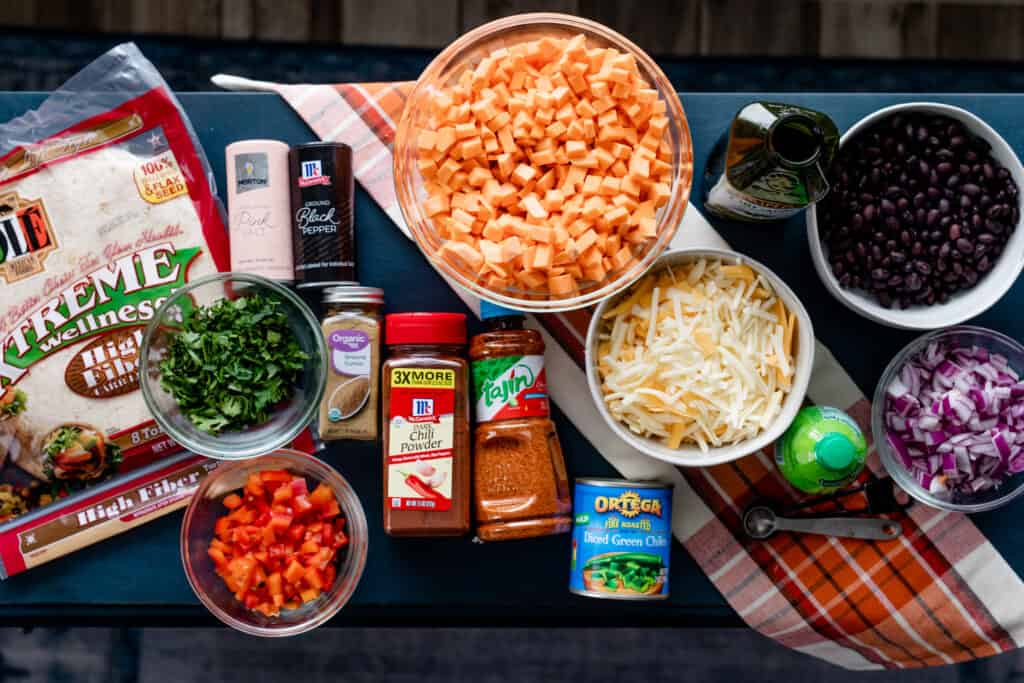 All of the ingredients and spices sit on a countertop ready to make sweet potato and black bean burritos.