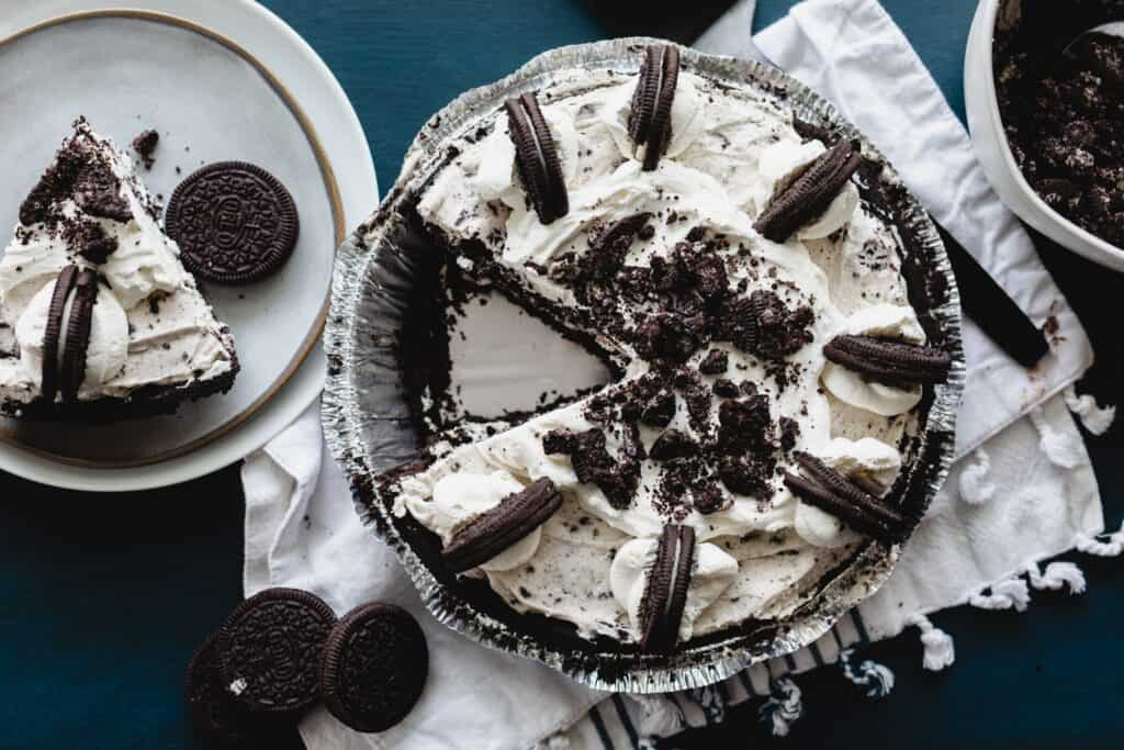 An Oreo cheesecake pie sits on the counter with a slice alongside it on a plate ready to serve.