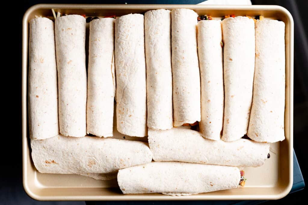 Wrapped burritos are laid out on a sheet pan ready to be baked.