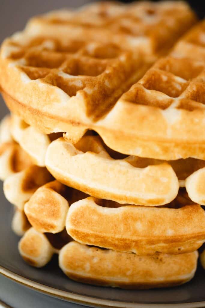 A stack of golden brown buttermilk waffles sit on a plate ready to be served.