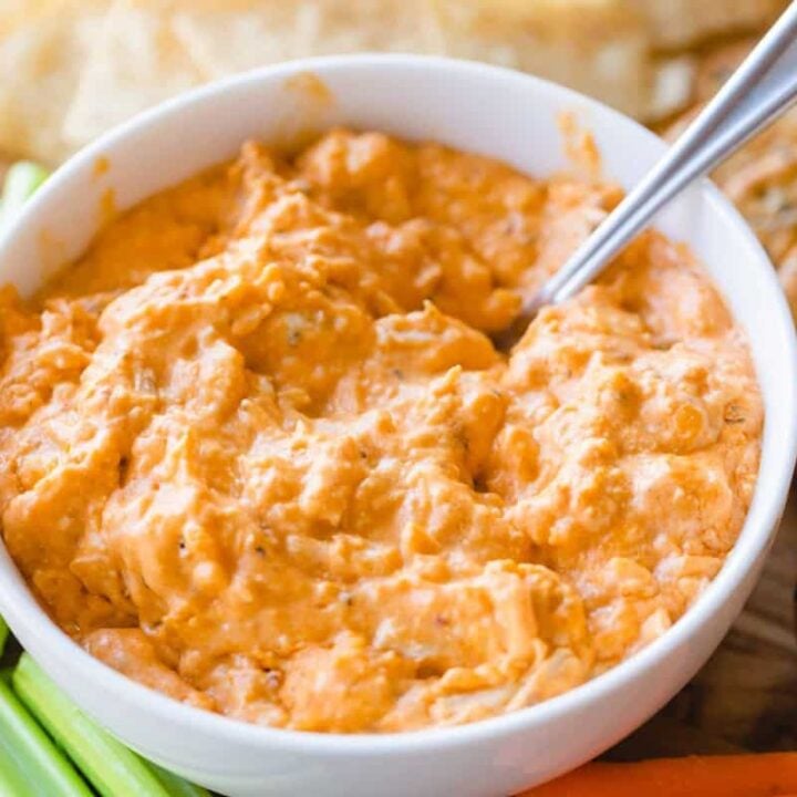 A white bowl filled with baked buffalo chicken dip sits surrounded by celery and crackers.
