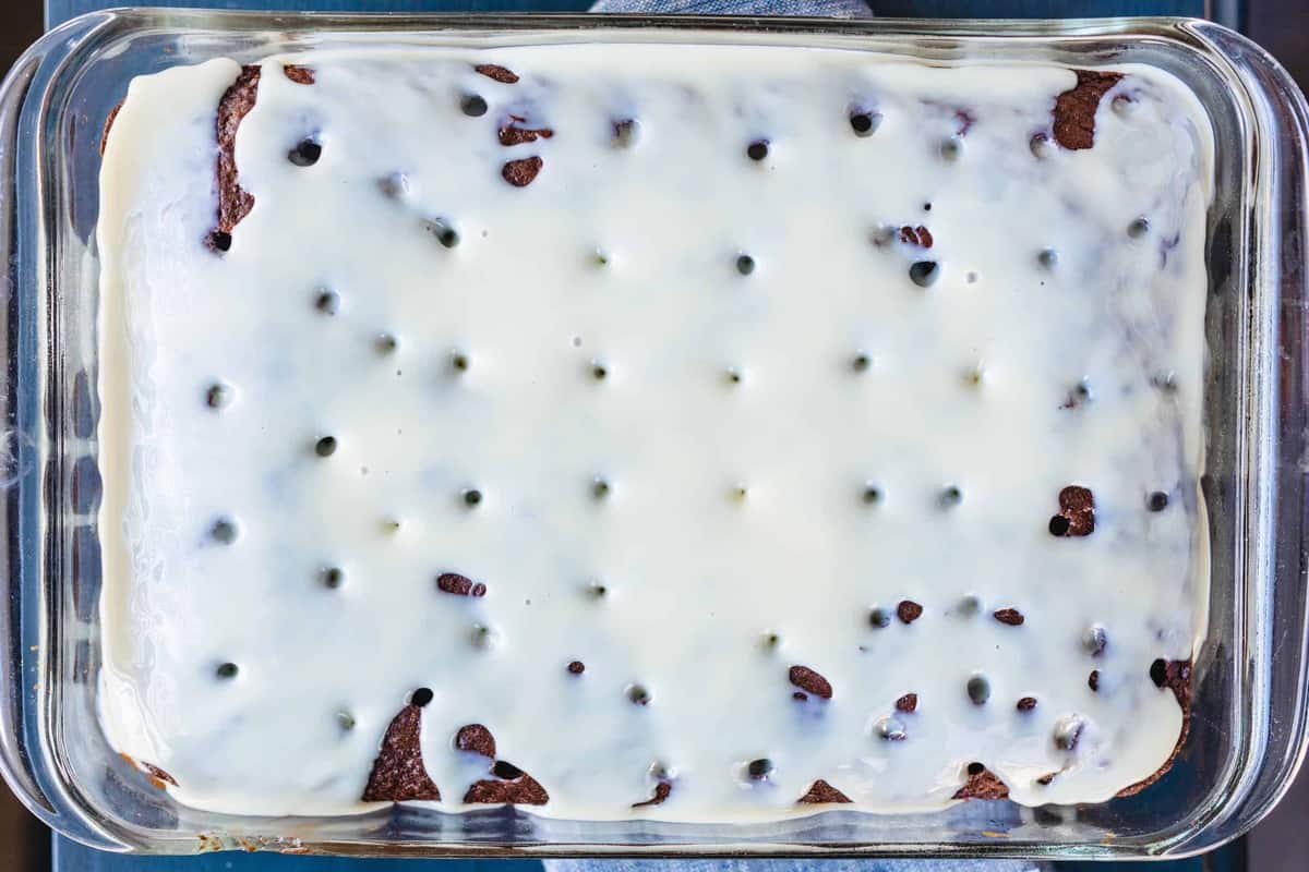 Sweetened Condensed Milk has been poured across the top of a chocolate cake with holes poked in it.