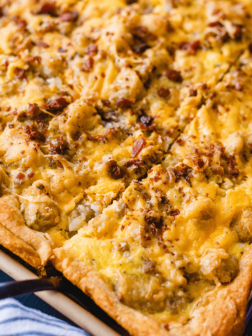 A spatuala sits under a square slice of breakfast pizza in a baking sheet.