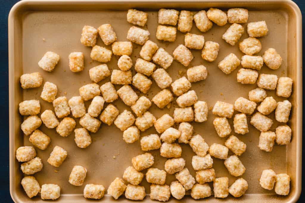 Frozen tater tots are scattered on a baking sheet.