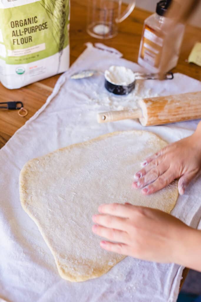 Ashley spreads out dough for homemade pasta on a bread cloth.