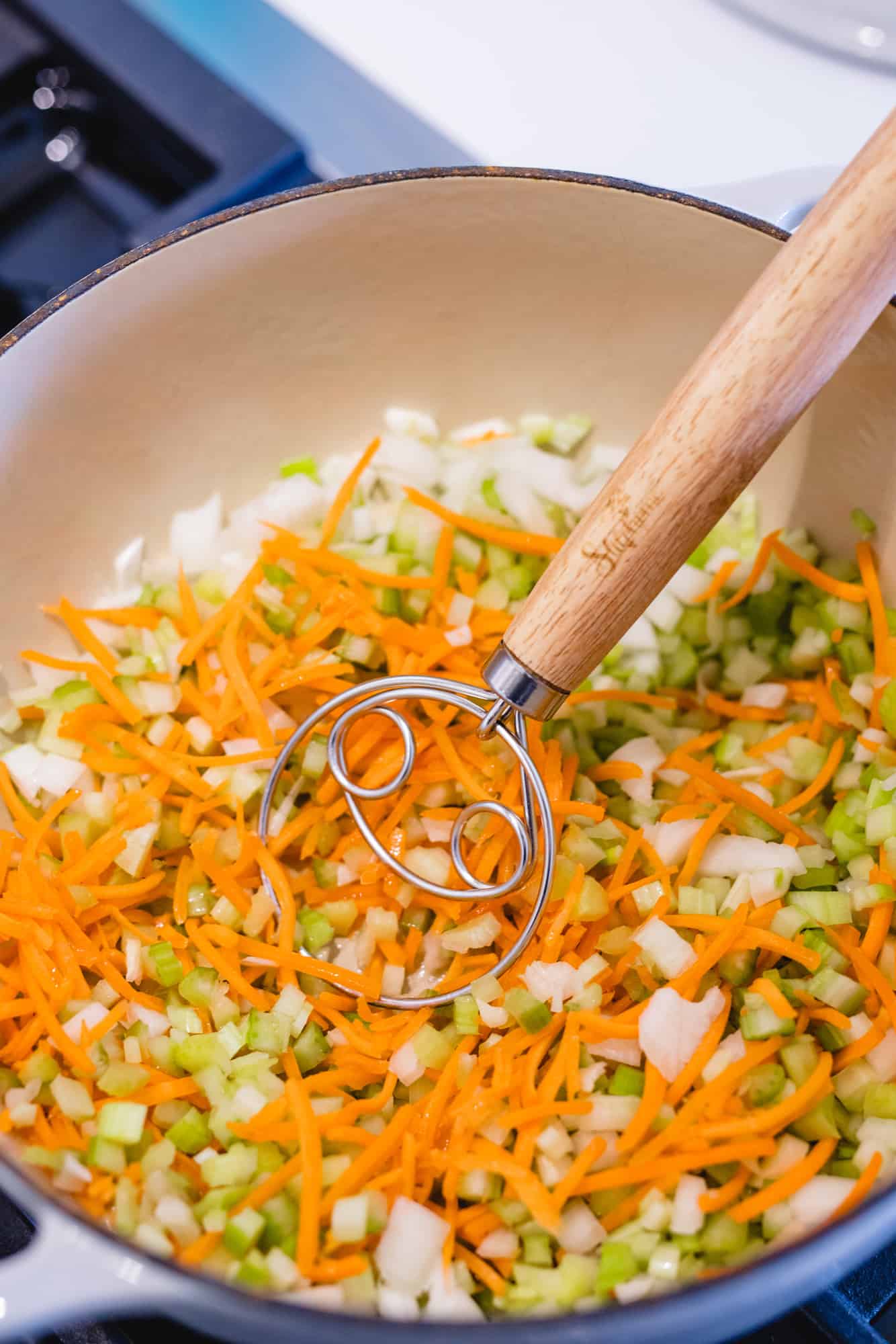 Diced carrots, celery, and onions sit in a pot to be sautéed.