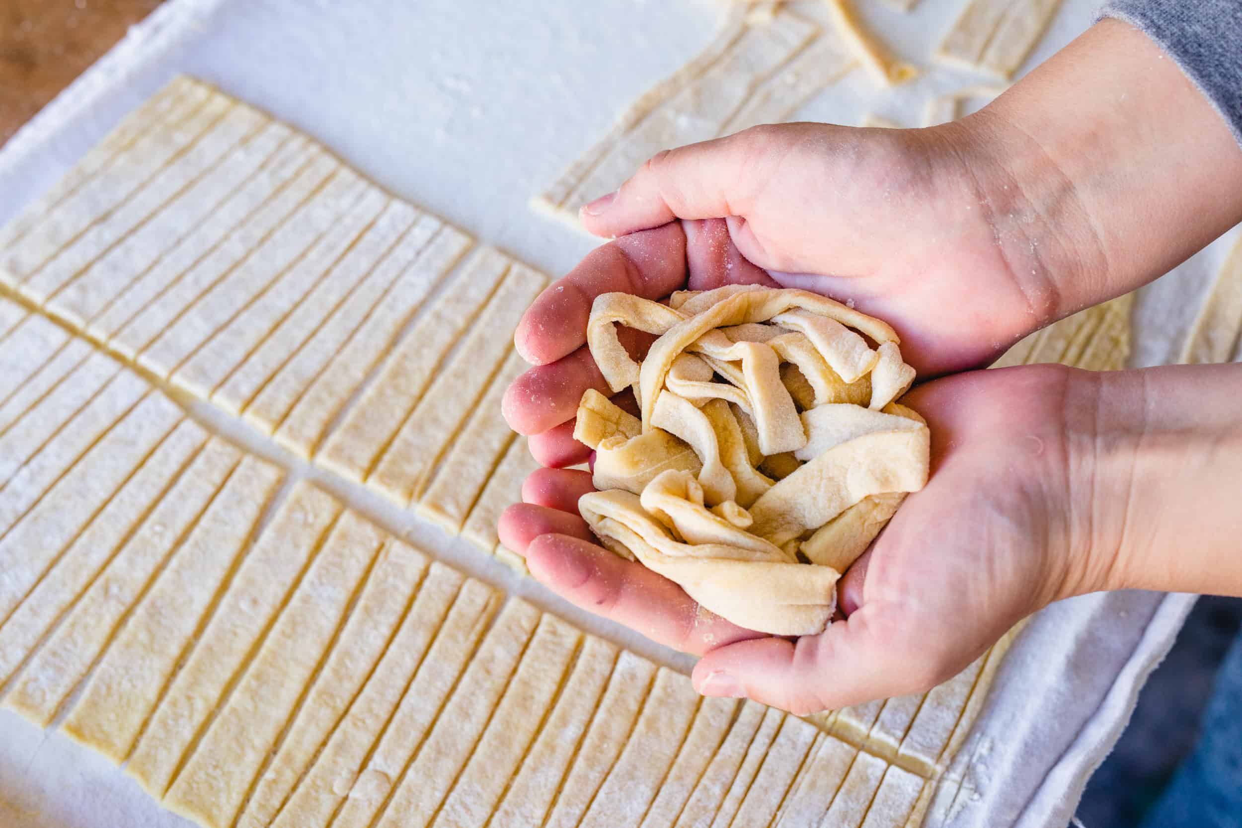 Ashley holds fresh cut egg noodles in the palms of her hands.