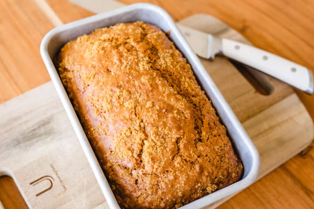 Golden brown loaf of banana bread, fresh from the oven cooks on a wooden cutting board.