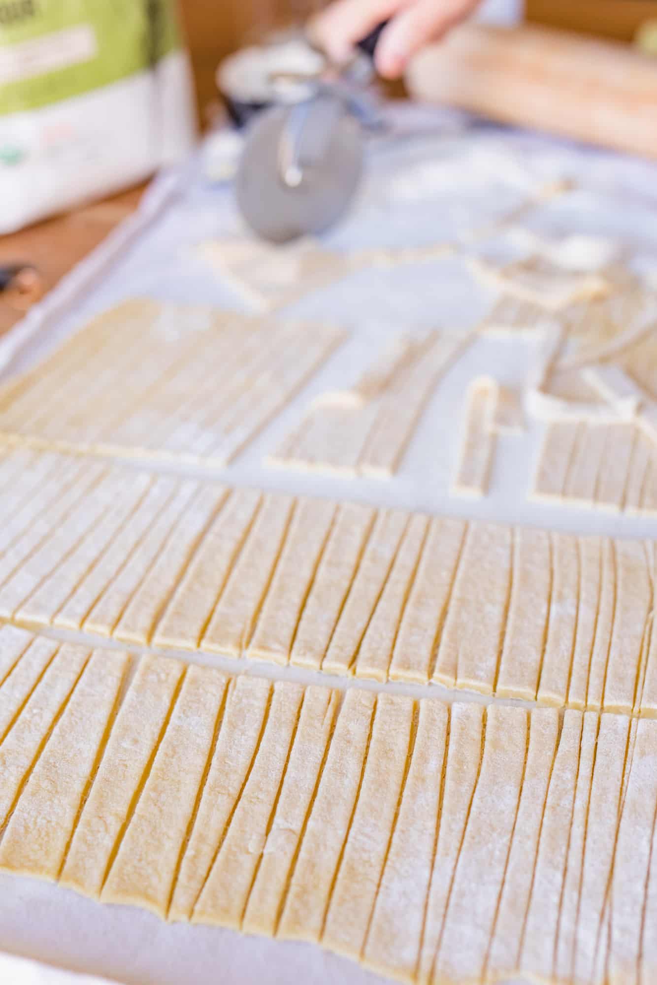 Using a pizza cutter Ashley slices fresh rolled out pasta dough for egg noodles.