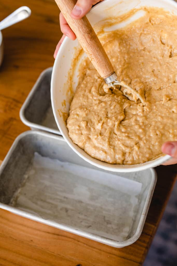 Ashley uses a dough whisk to transfer banana bread batter to a parchment lined bread pan.
