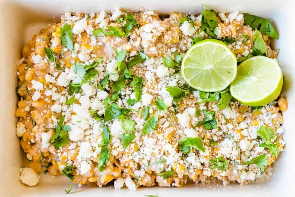 Mexican salad is topped with fresh limes and cilantro sits in a white serving dish.