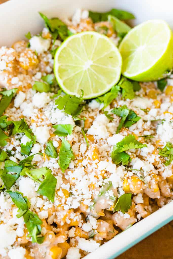Mexican Street Corn Salad in a white casserole dish topped with cotija cheese and limes.