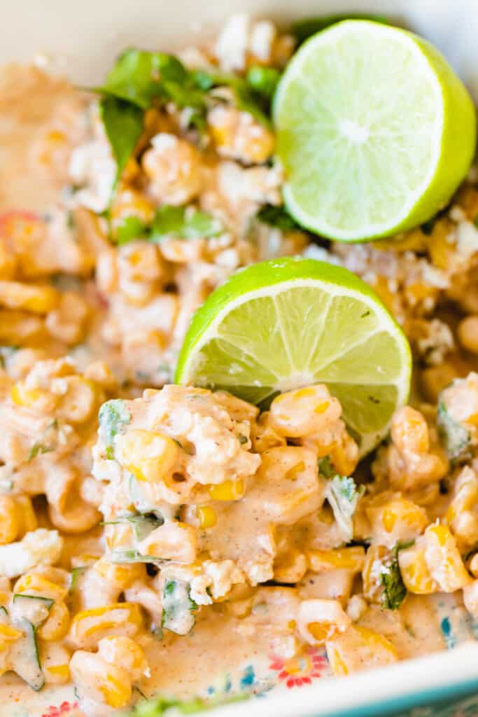 Mexican corn salad sits in a white casserole dish topped with limes.