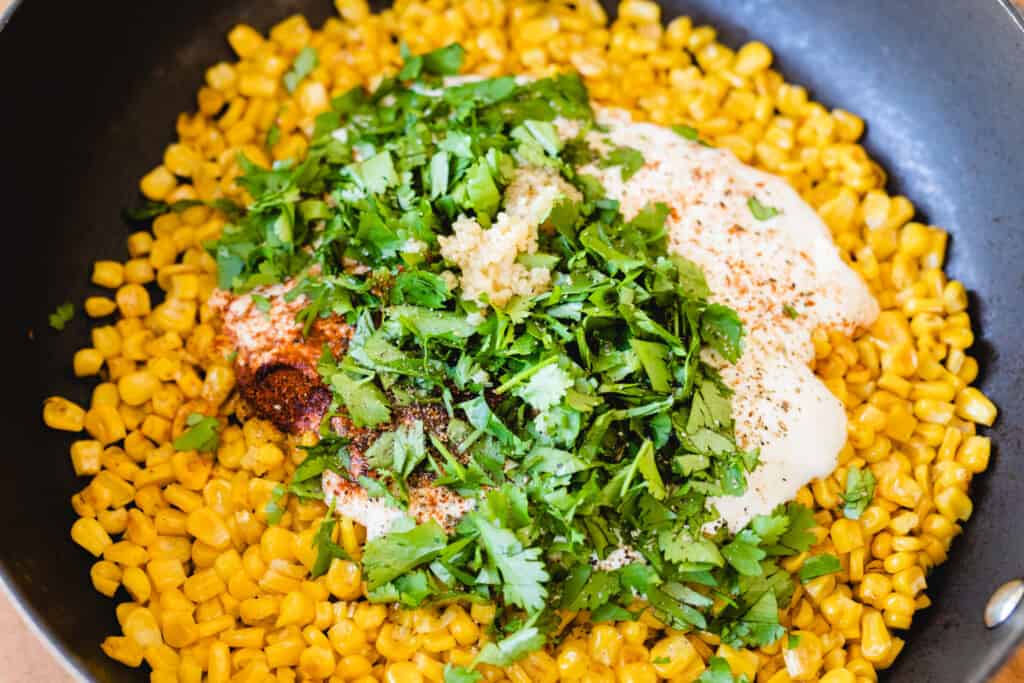 Charred corn, crema, cilantro, and minced garlic sit in a pan over the stove.