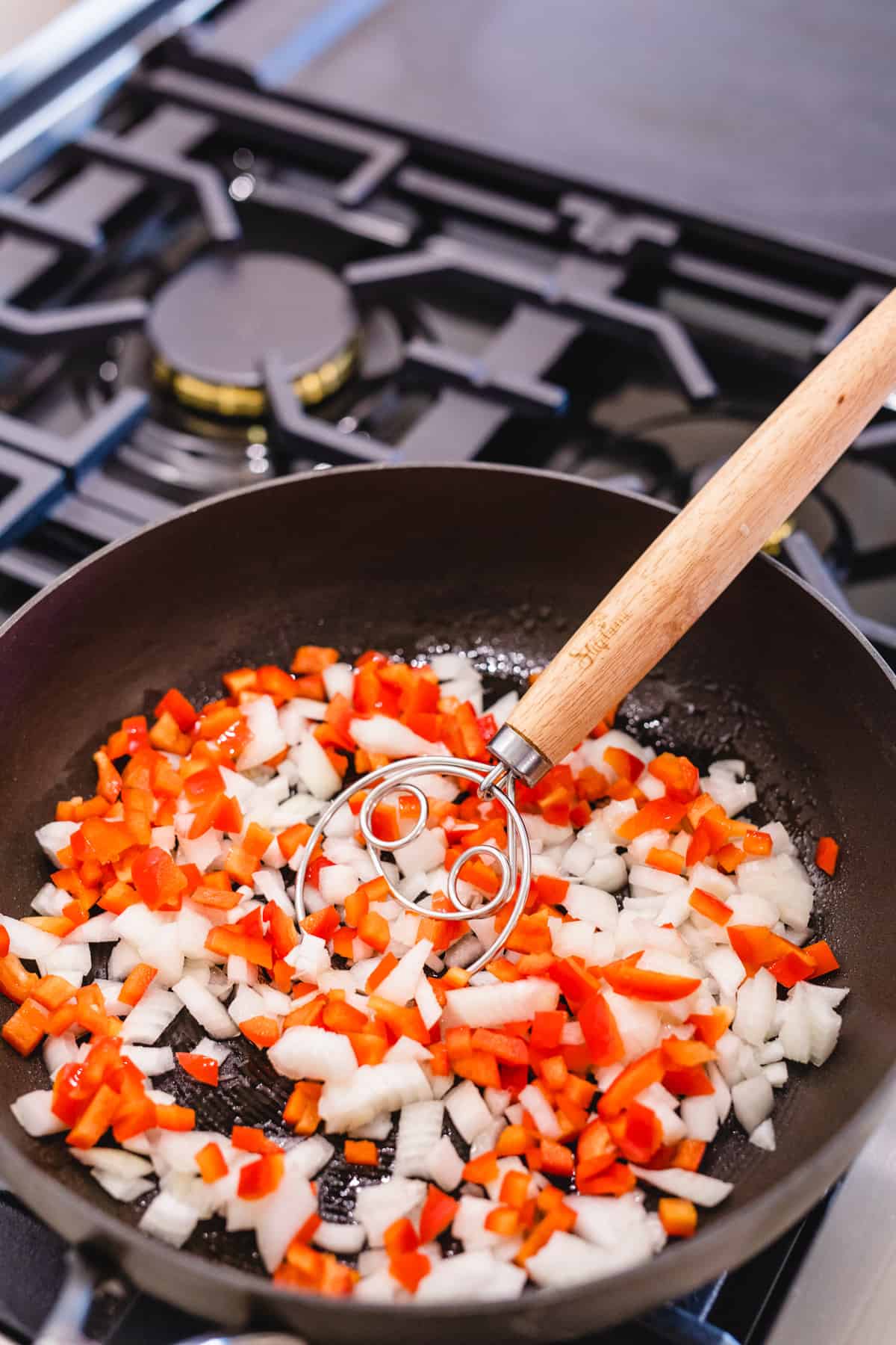 Chopped onion and red pepper sits in a pan on top of a stove.
