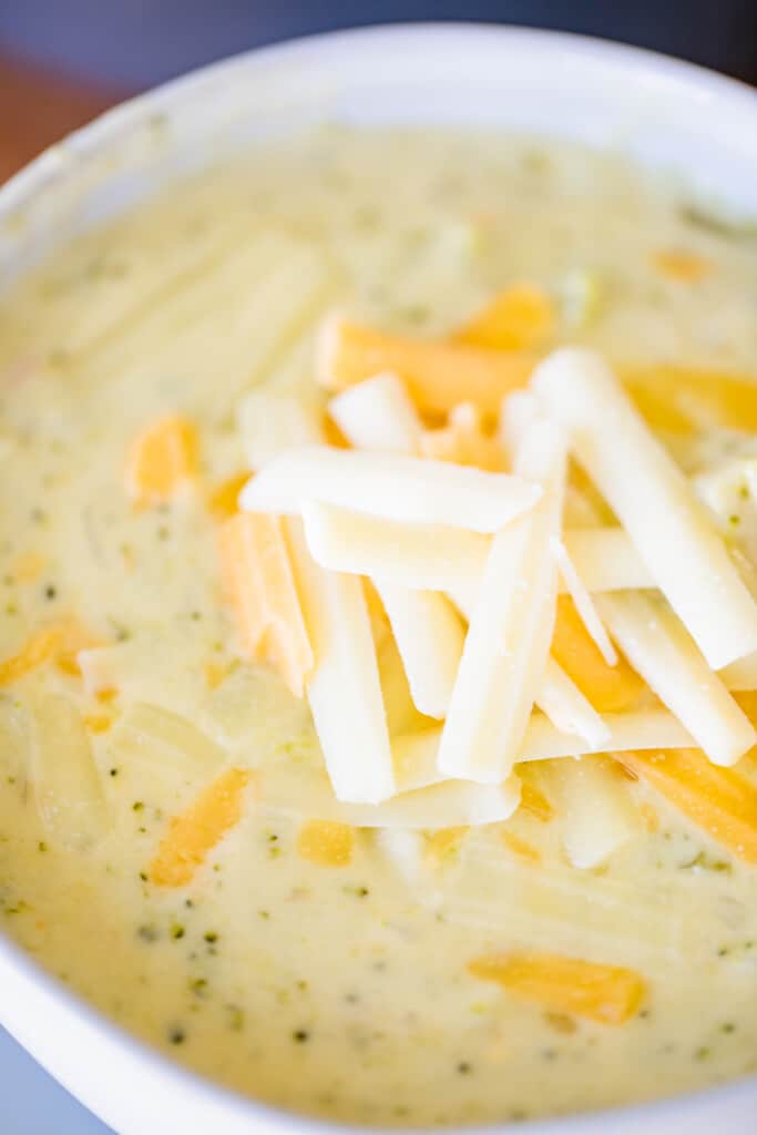 Bowl of cheddar broccoli soup is topped with shredded cheese.