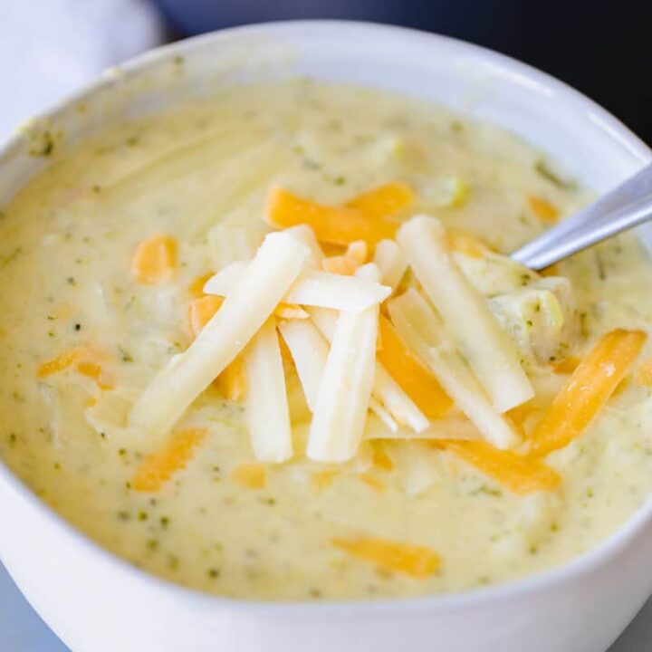 Bowl of cheesy vegetable soup sits on a plate.