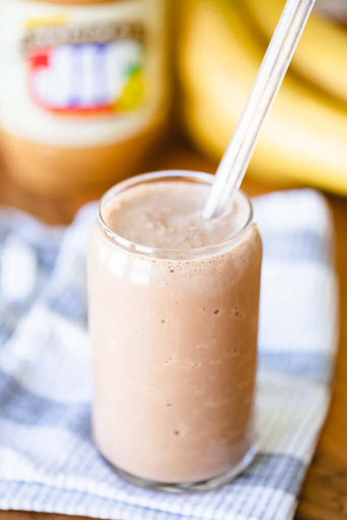 Healthy smoothie sits in a tall glass with peanut butter and banana sitting behind.