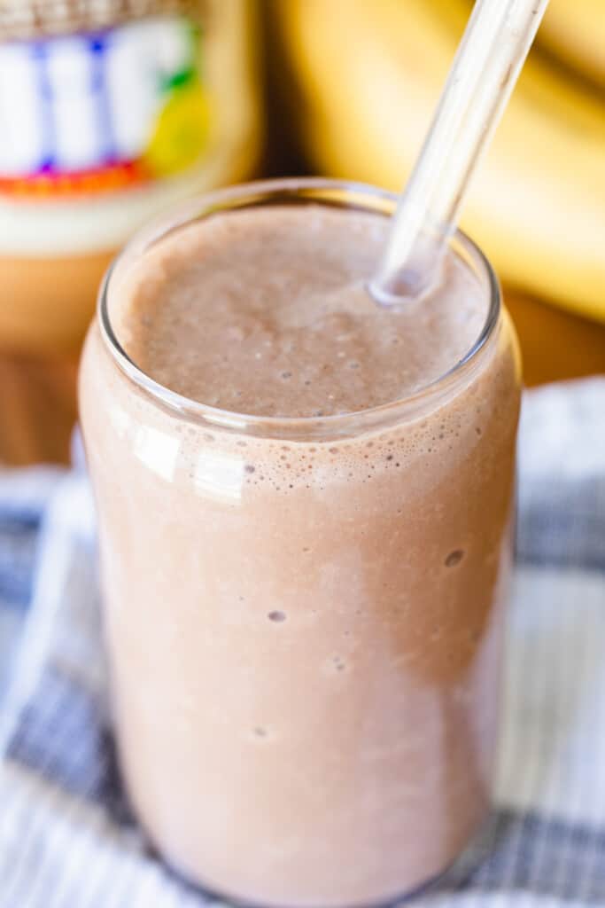 A clear straw sits in a glass full of healthy chocolate smoothie.