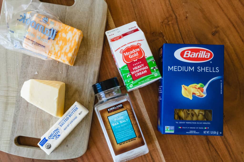 Ingredients for stovetop mac and cheese lay out on the counter to prepare recipe. Shell pasta, sea salt, cream, butter, and two kinds of cheese.