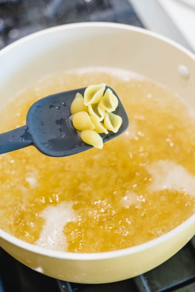 A black spatula lifts cooked pasta from a pot of boiling water.