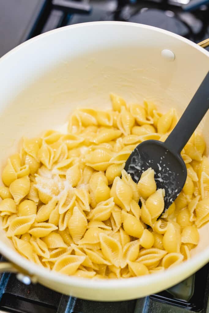 Cooked pasta sits in a pot over the stove with a black spatula being used for stirring.