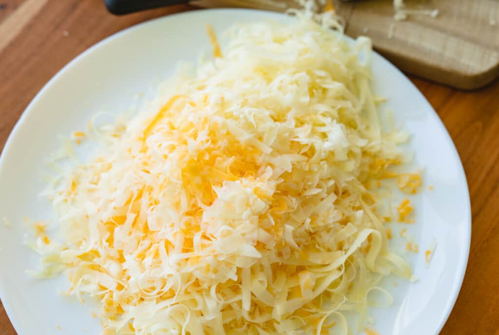 A pile of freshly grated cheeses sits on a white plate.