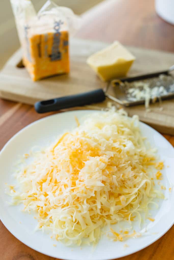 Two blocks of freshly grated colby jack and white cheddar cheese sit on a white plate for adding to stovetop mac and cheese.