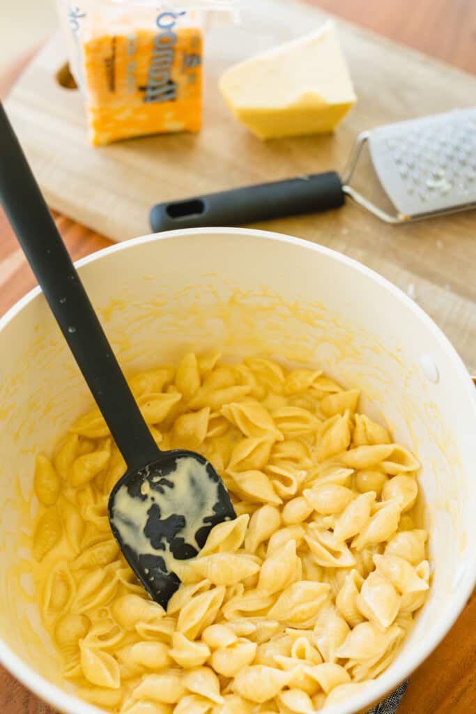 A large spatula stirs a pot of creamy noodles in a rich cheese sauce.