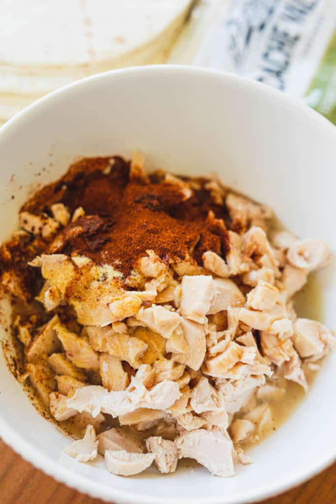Seasonings, honey, lime juice are added to a white bowl with shredded chicken.