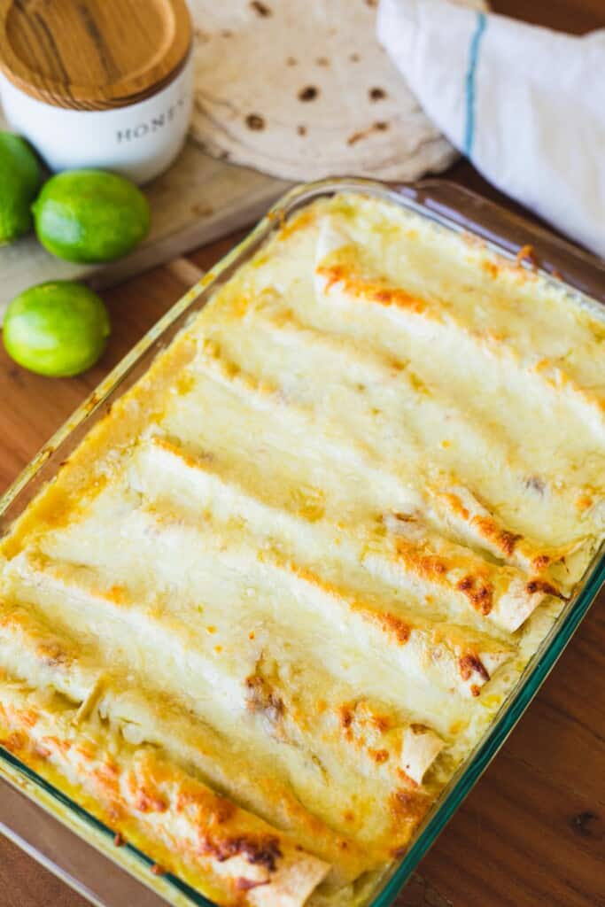 Large glass pan of cheesy baked honey lime chicken enchiladas sit on a counter.