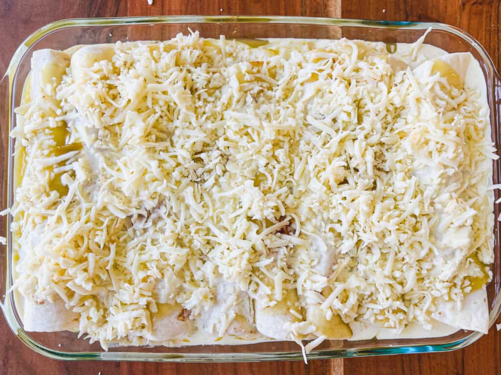 Shredded cheese is added to the top of a pan of prepared enchiladas.