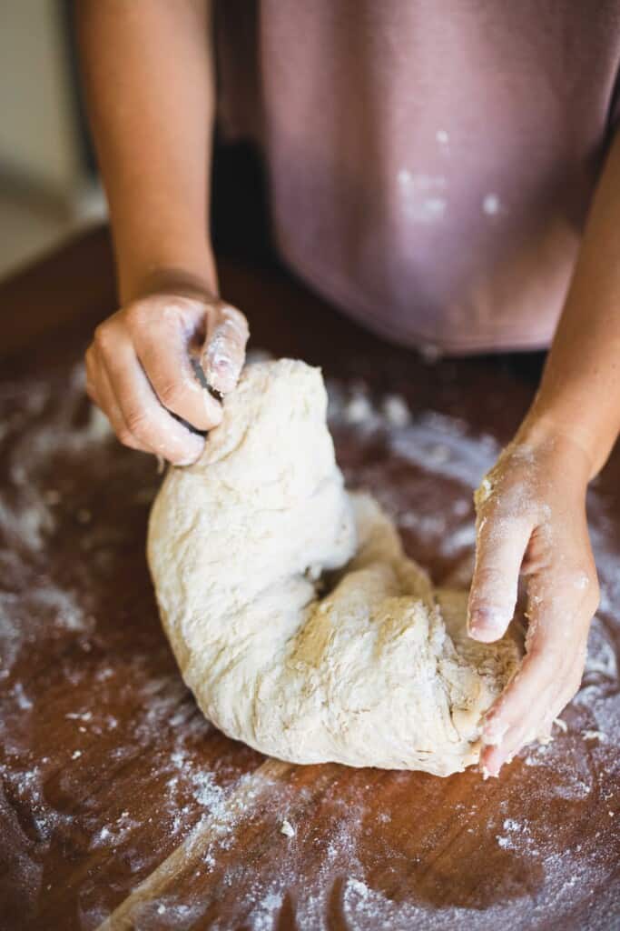 Ashley works a ball of homemade bread dough on a wooden counter.