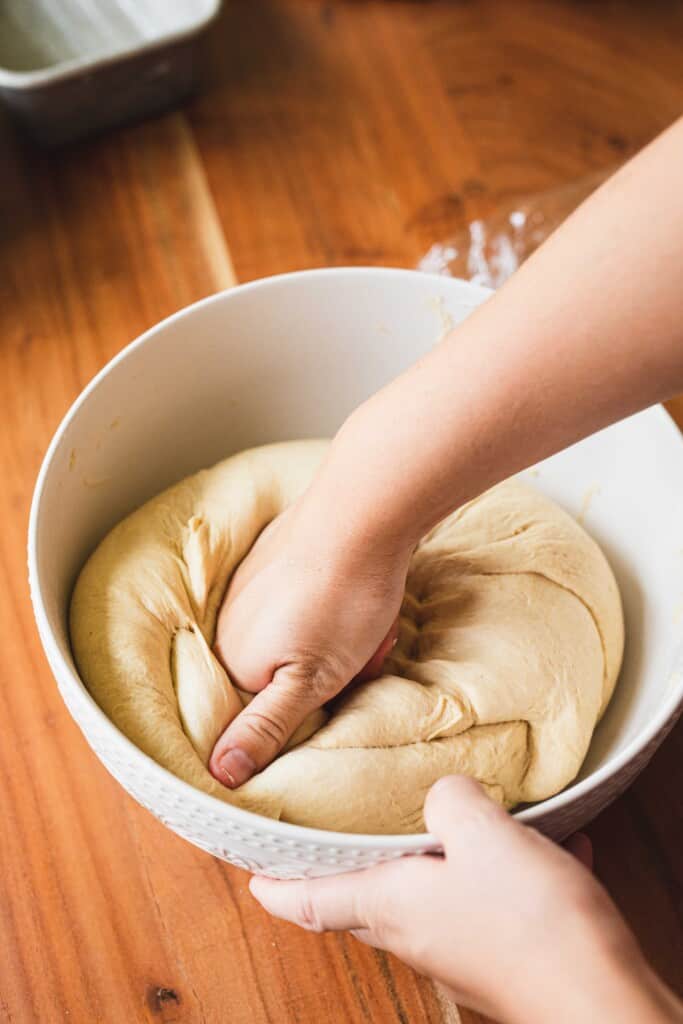 Ashley punches down raised bread dough in a white ceramic bowl.