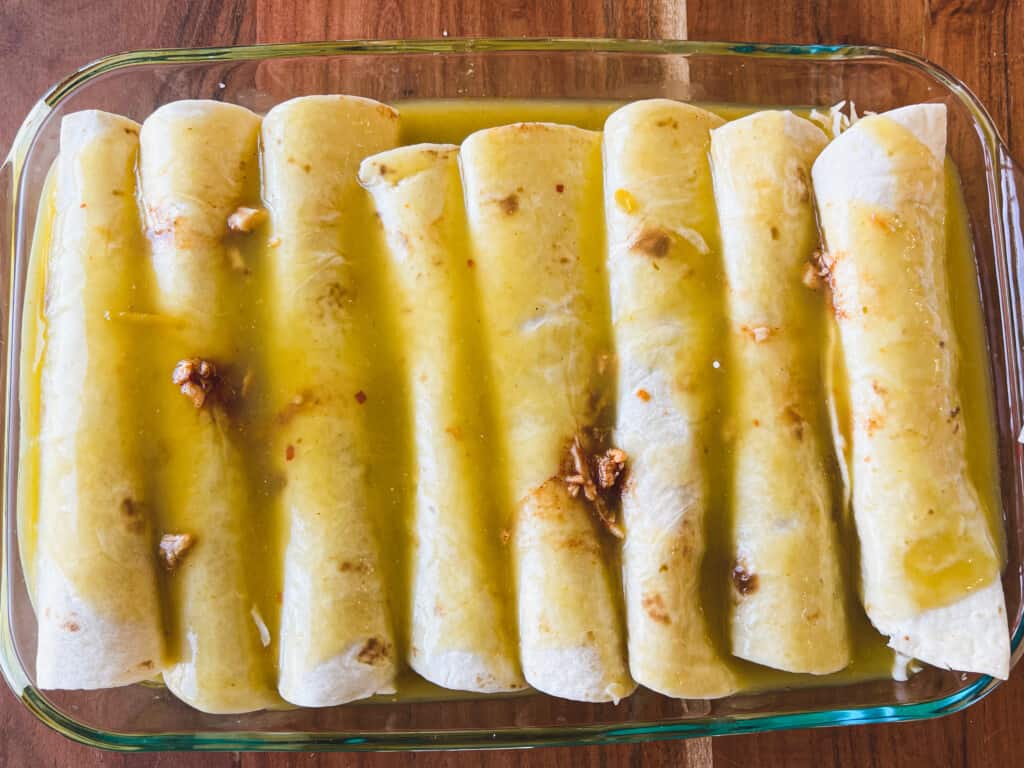 Green enchilada sauce is poured over the top of rolled and filled tortillas.
