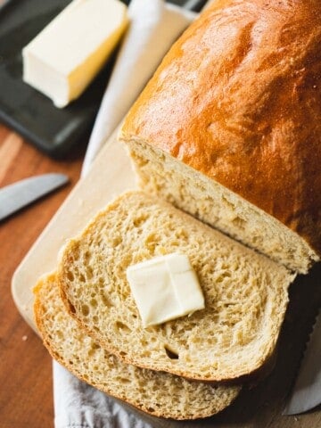 A pat of butter sits on a slice of fresh sliced bread.