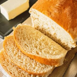 Three thick slices of homemade bread have been cut over a wooden cutting board.