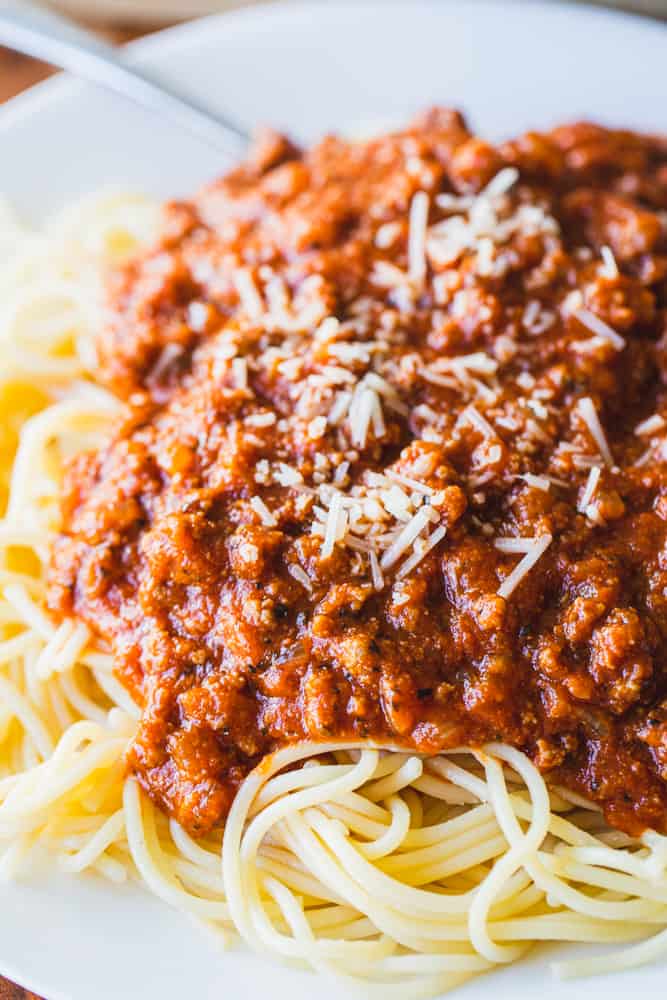 A white plate is filled with spaghetti and meat sauce.